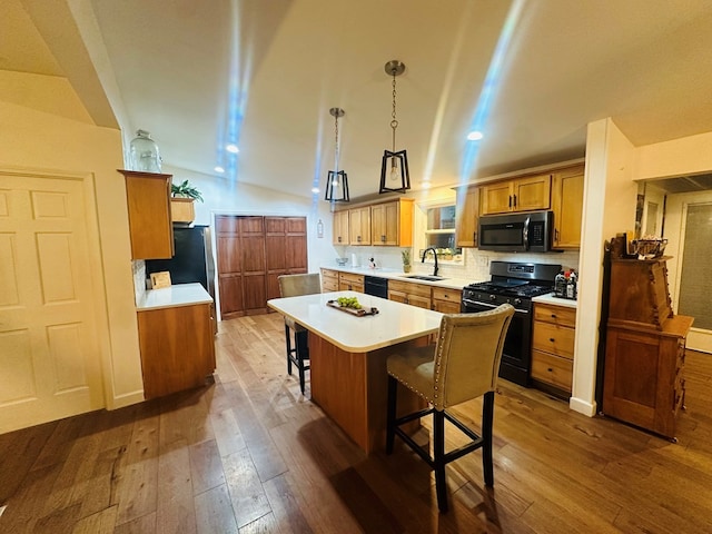 kitchen featuring black appliances, decorative light fixtures, a kitchen bar, wood-type flooring, and sink