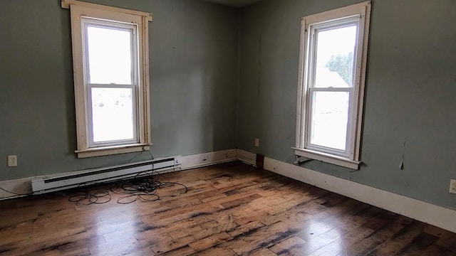 spare room featuring a baseboard radiator, a healthy amount of sunlight, and dark wood-type flooring