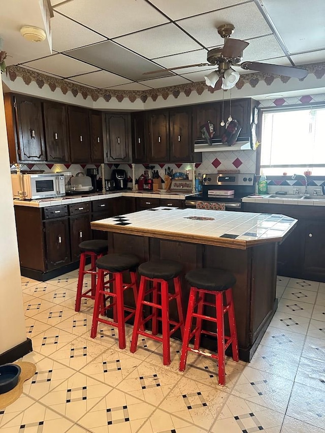 kitchen featuring a kitchen bar, dark brown cabinets, sink, tile countertops, and stainless steel electric range oven