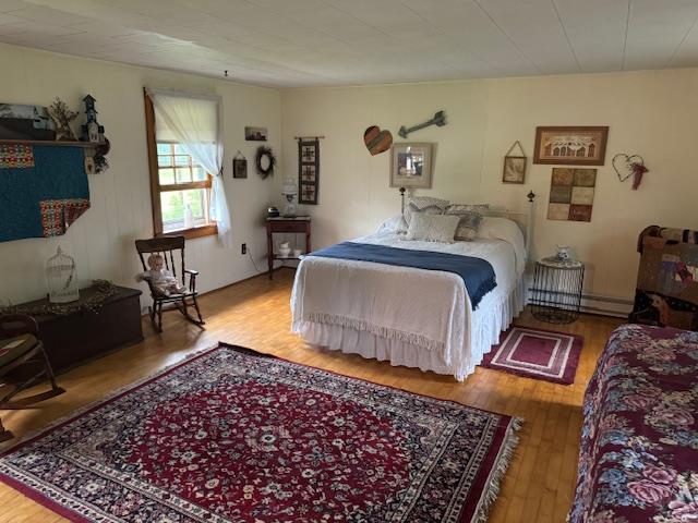 bedroom featuring hardwood / wood-style floors and a baseboard heating unit