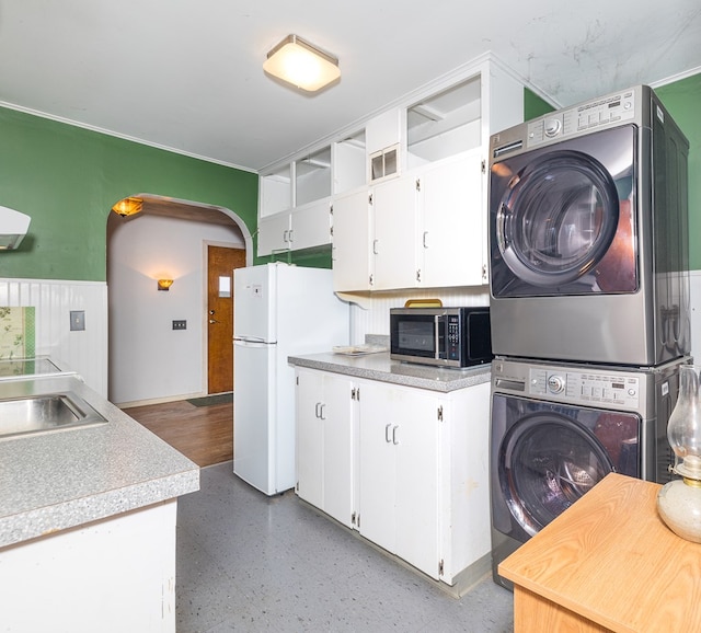 kitchen with white refrigerator, stacked washer and dryer, sink, and white cabinets