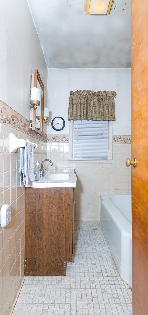 bathroom with tile walls, vanity, tile patterned flooring, and a tub