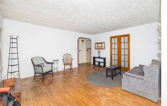 sitting room featuring arched walkways, wood finished floors, a textured ceiling, french doors, and baseboards