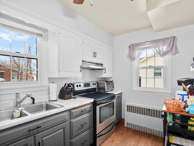 kitchen featuring electric range, gray cabinetry, white cabinets, radiator, and under cabinet range hood