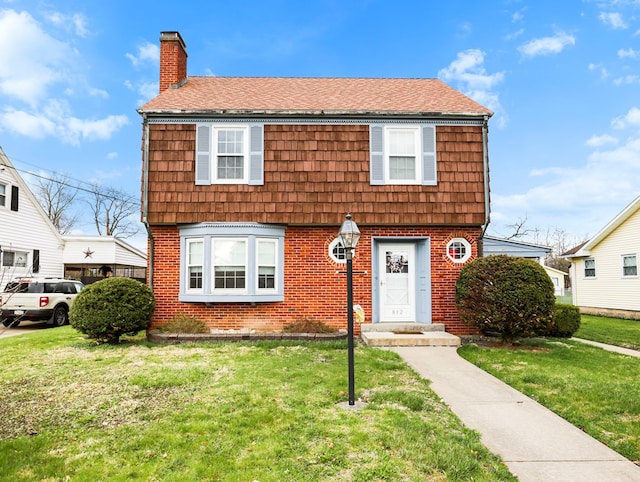 colonial inspired home featuring brick siding, a front yard, and a chimney