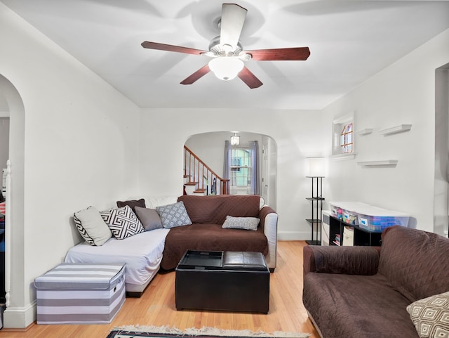 living area featuring stairs, wood finished floors, baseboards, ceiling fan, and arched walkways