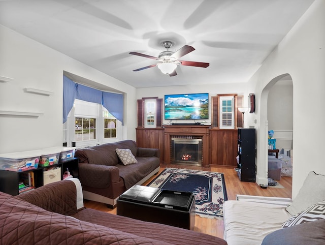 living room with arched walkways, ceiling fan, a fireplace with flush hearth, and wood finished floors