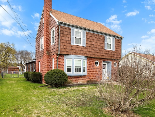 colonial inspired home featuring a front lawn, fence, roof with shingles, a chimney, and brick siding