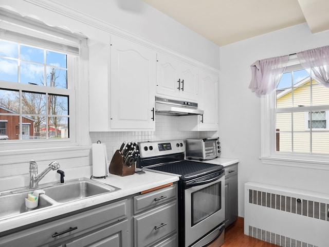 kitchen featuring gray cabinets, electric range, a sink, radiator heating unit, and under cabinet range hood