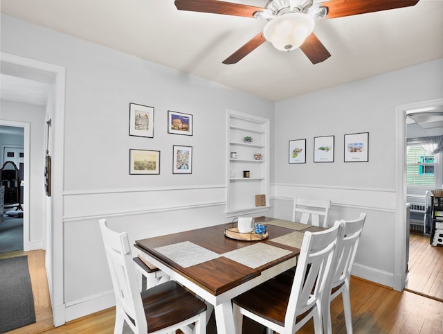 dining area with light wood-type flooring, built in features, and ceiling fan