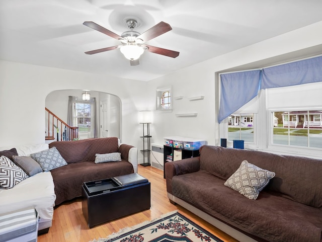 living area featuring ceiling fan, light wood finished floors, arched walkways, radiator, and stairway