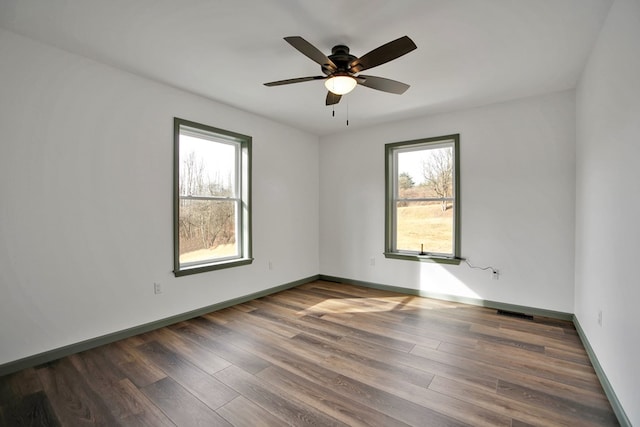 empty room featuring dark wood-type flooring, ceiling fan, and a healthy amount of sunlight