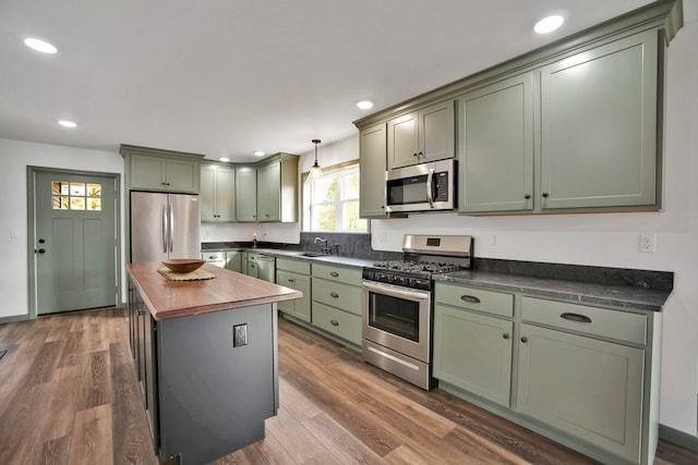 kitchen featuring butcher block countertops, hanging light fixtures, green cabinetry, and appliances with stainless steel finishes