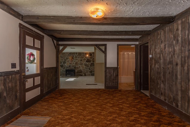 interior space featuring carpet flooring, beam ceiling, and a wood stove