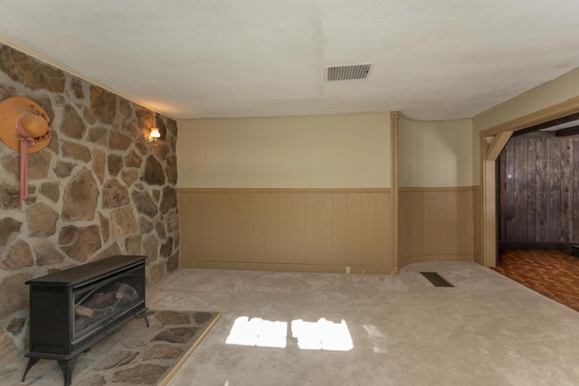 unfurnished living room featuring light carpet, wooden walls, and a wood stove