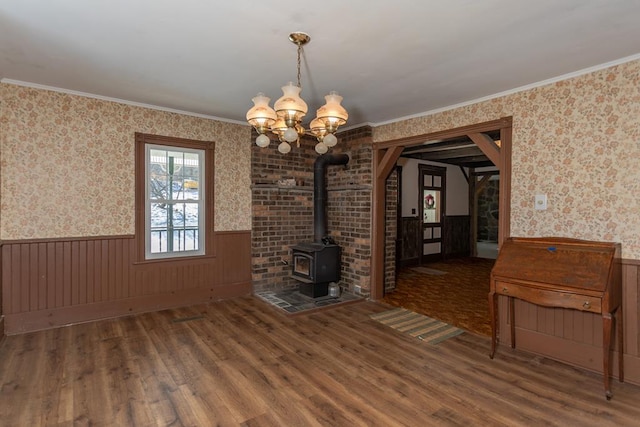 unfurnished living room with a notable chandelier, crown molding, wood-type flooring, and a wood stove