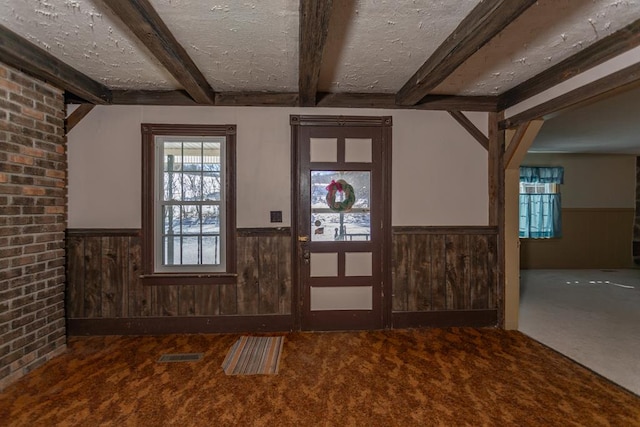 carpeted entrance foyer with beam ceiling, wooden walls, and a textured ceiling