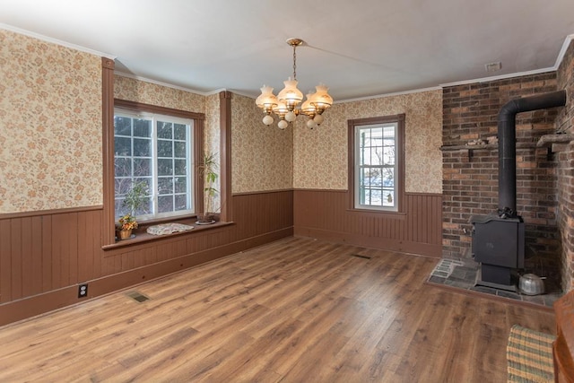 unfurnished dining area featuring a notable chandelier, ornamental molding, wood-type flooring, and a wood stove