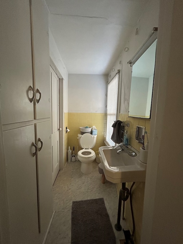 half bath with wainscoting, tile walls, toilet, and a sink