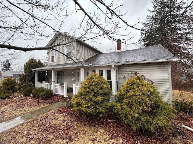 view of front facade with covered porch, a chimney, and a shingled roof