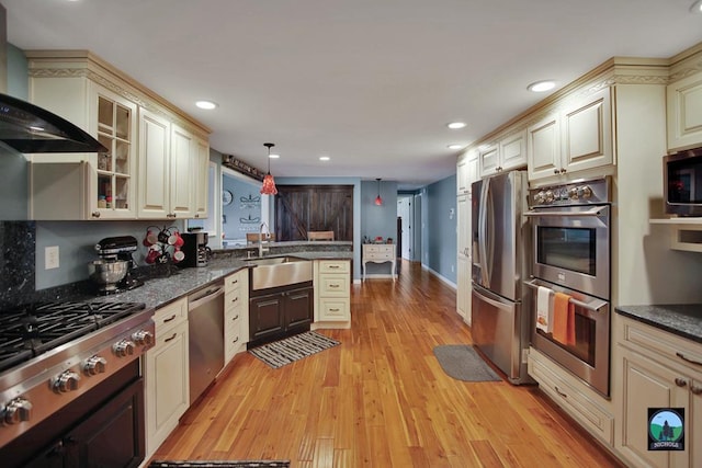 kitchen featuring cream cabinets, wall chimney range hood, sink, hanging light fixtures, and appliances with stainless steel finishes