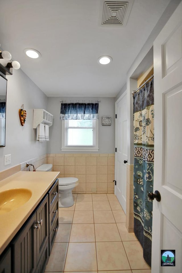 bathroom featuring toilet, vanity, tile patterned floors, and tile walls