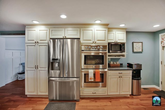 kitchen with cream cabinets, light wood-type flooring, stainless steel appliances, and dark stone counters