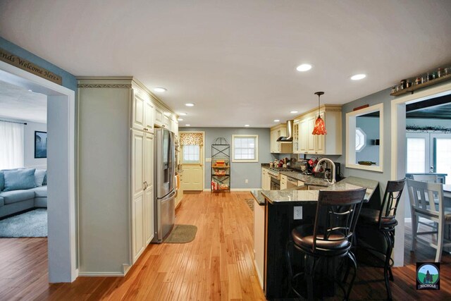 kitchen featuring hanging light fixtures, light hardwood / wood-style flooring, kitchen peninsula, stainless steel fridge, and a kitchen bar