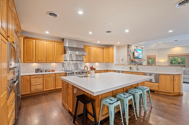 kitchen with decorative backsplash, a kitchen breakfast bar, wall chimney exhaust hood, sink, and a center island with sink