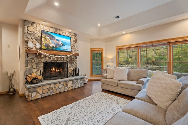 living room with a raised ceiling, dark hardwood / wood-style flooring, and a stone fireplace