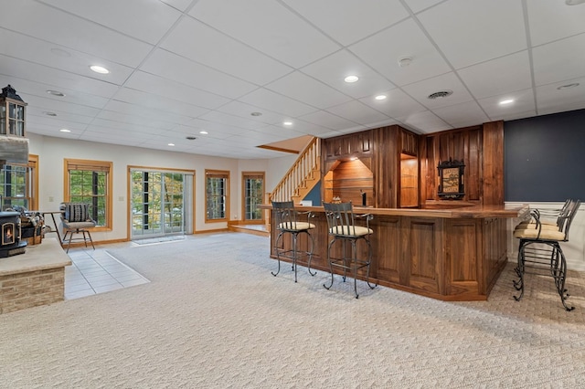 bar with a wood stove, wood walls, a drop ceiling, and light colored carpet