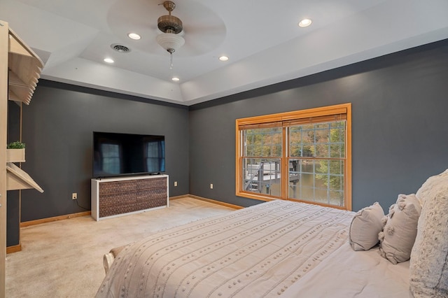 bedroom with light colored carpet, a raised ceiling, and ceiling fan