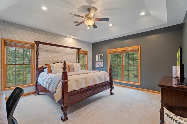 carpeted bedroom featuring a raised ceiling, ceiling fan, and brick wall