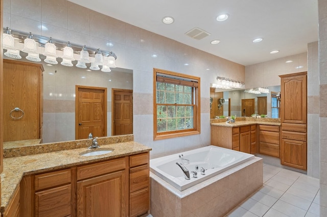 bathroom with tiled tub, tile patterned flooring, vanity, and tile walls