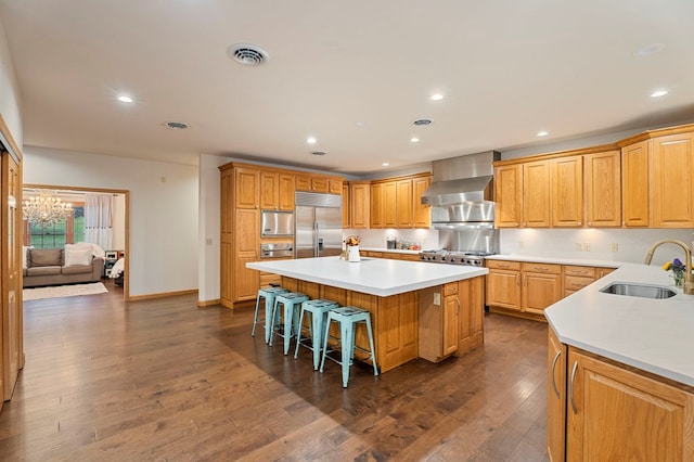 kitchen featuring a breakfast bar, sink, built in refrigerator, wall chimney exhaust hood, and a kitchen island