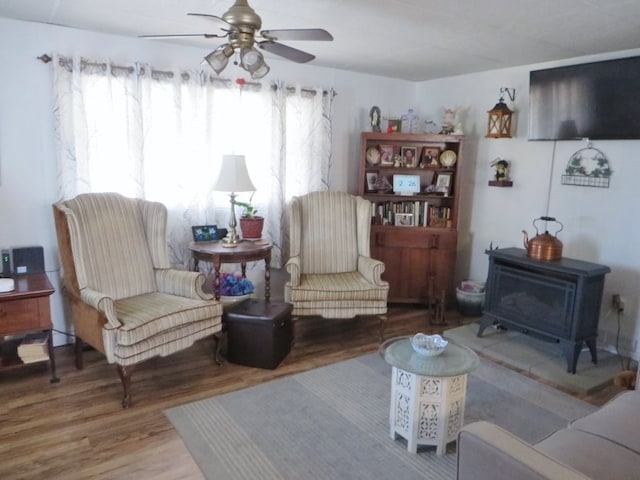 living area with a wood stove, wood finished floors, and a ceiling fan