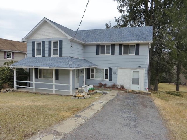 view of front of home featuring driveway, a porch, a front lawn, and a shingled roof