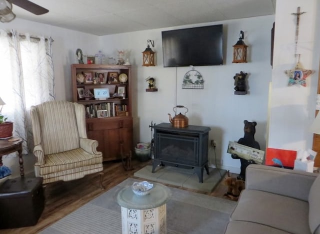 living room featuring a ceiling fan, wood finished floors, and a wood stove