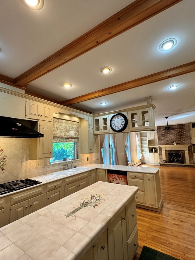 kitchen featuring tile countertops, stainless steel gas stovetop, decorative backsplash, beamed ceiling, and light hardwood / wood-style floors