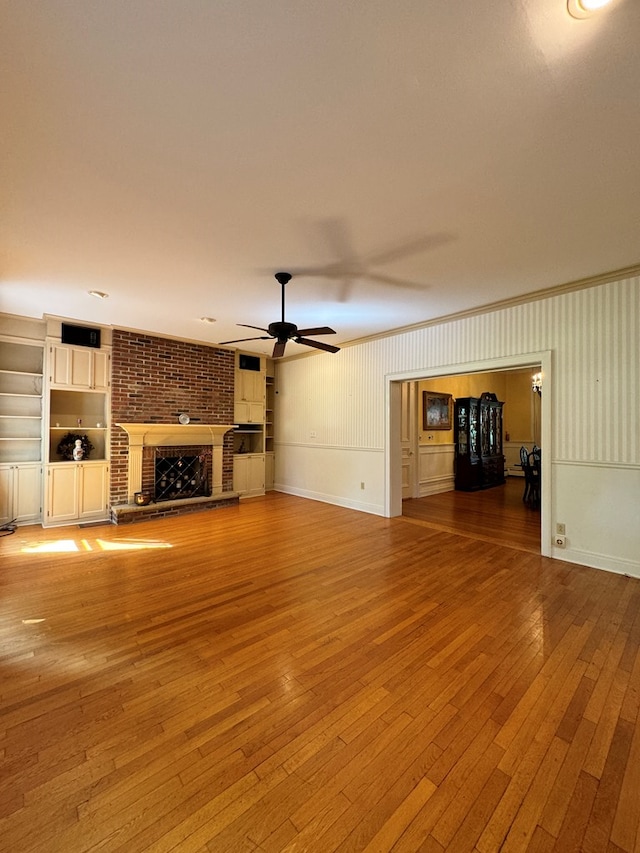 unfurnished living room featuring ceiling fan, a fireplace, built in features, and light wood-type flooring