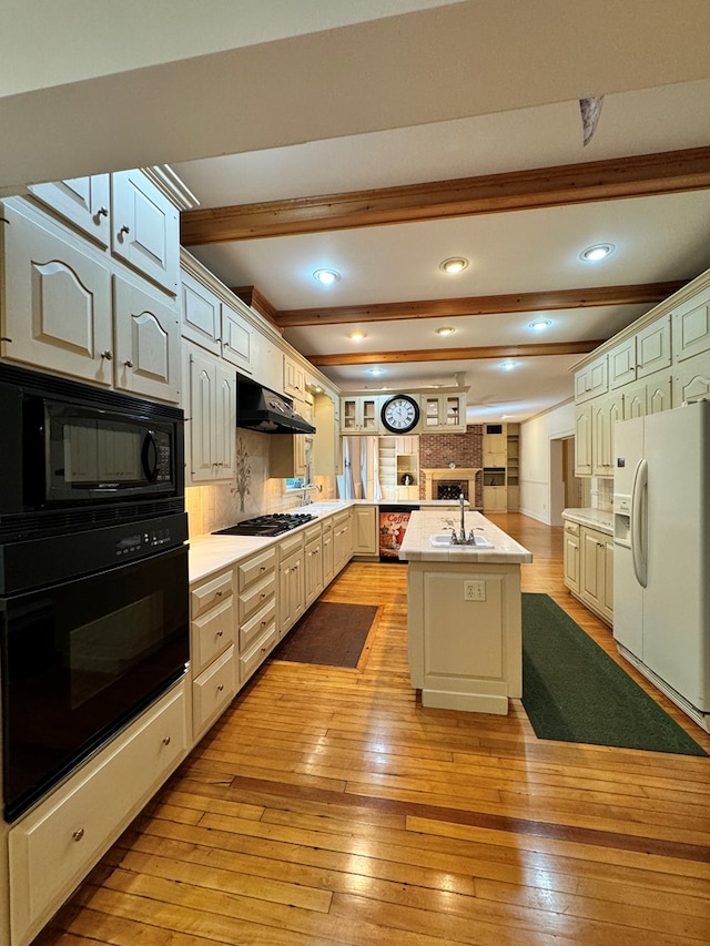 kitchen featuring beam ceiling, backsplash, light hardwood / wood-style floors, a kitchen island with sink, and black appliances