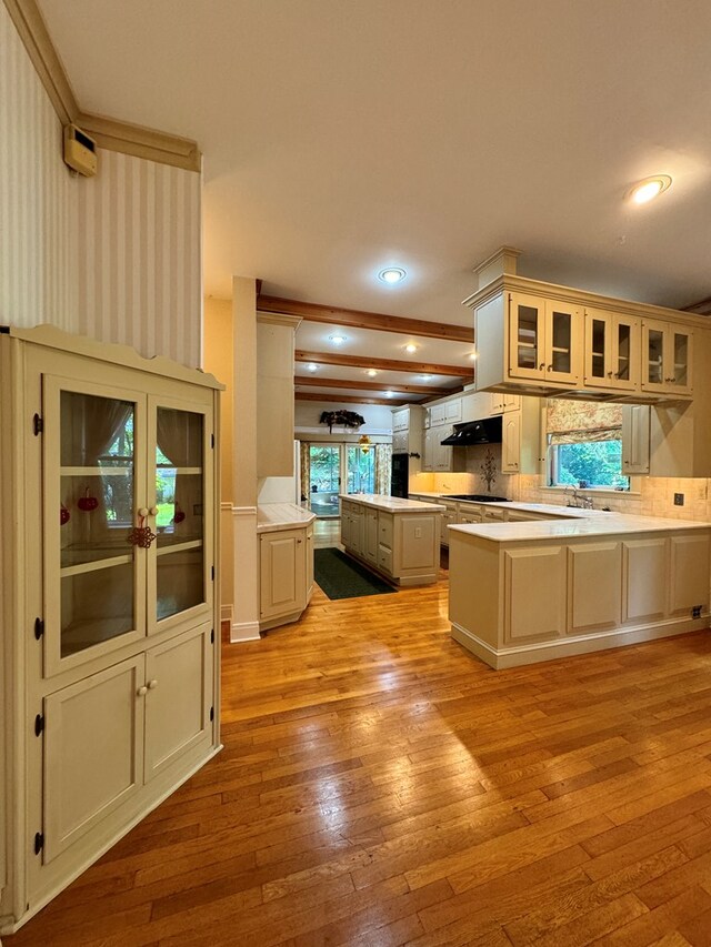 kitchen featuring cream cabinetry, light hardwood / wood-style floors, kitchen peninsula, and backsplash