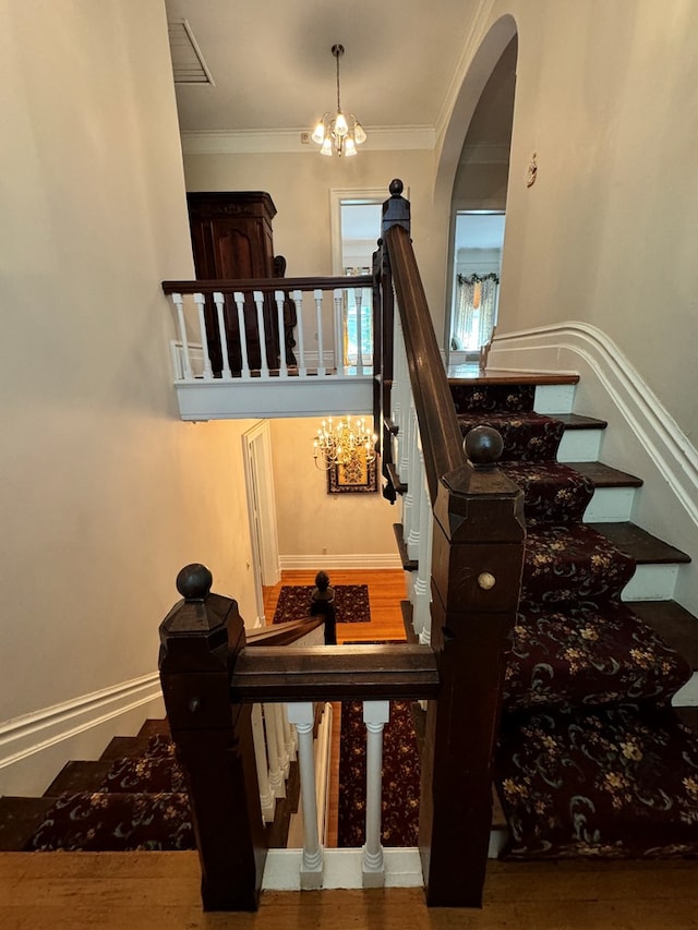 staircase with crown molding, wood-type flooring, and a notable chandelier