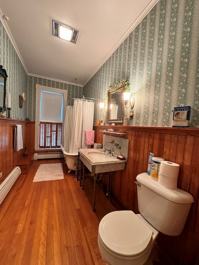 bathroom with hardwood / wood-style floors, wood walls, toilet, ornamental molding, and a baseboard radiator