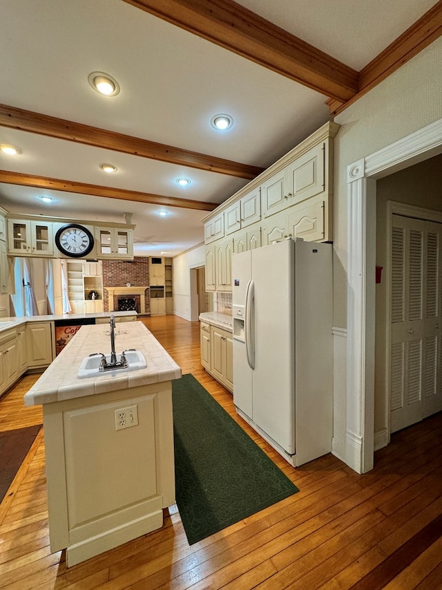 kitchen featuring sink, white refrigerator with ice dispenser, beam ceiling, tile countertops, and light hardwood / wood-style floors