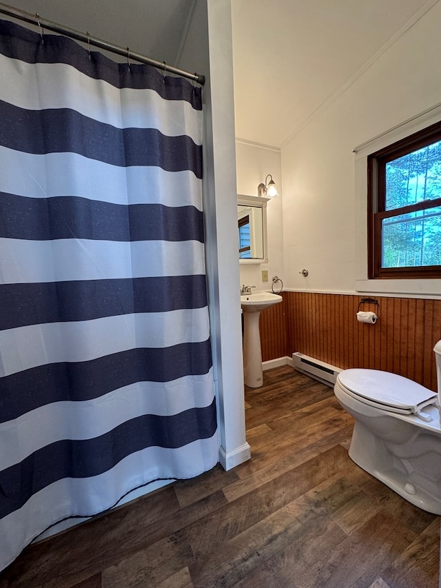 bathroom with toilet, sink, wood walls, hardwood / wood-style flooring, and a baseboard heating unit