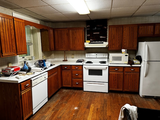 kitchen featuring under cabinet range hood, white appliances, light countertops, decorative backsplash, and dark wood finished floors