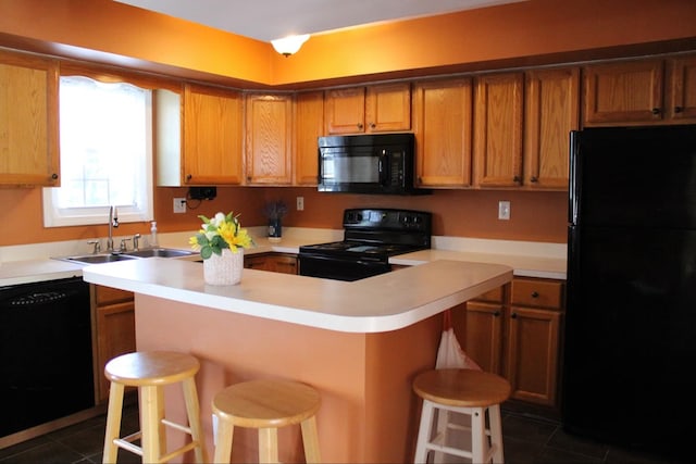 kitchen with black appliances, a kitchen bar, dark tile patterned floors, and sink