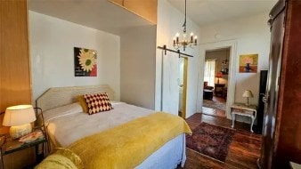 bedroom with a chandelier, a barn door, and dark wood-style flooring