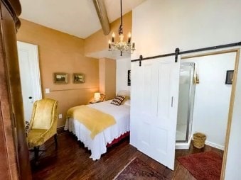 bedroom featuring a notable chandelier, dark hardwood / wood-style floors, lofted ceiling with beams, and a barn door